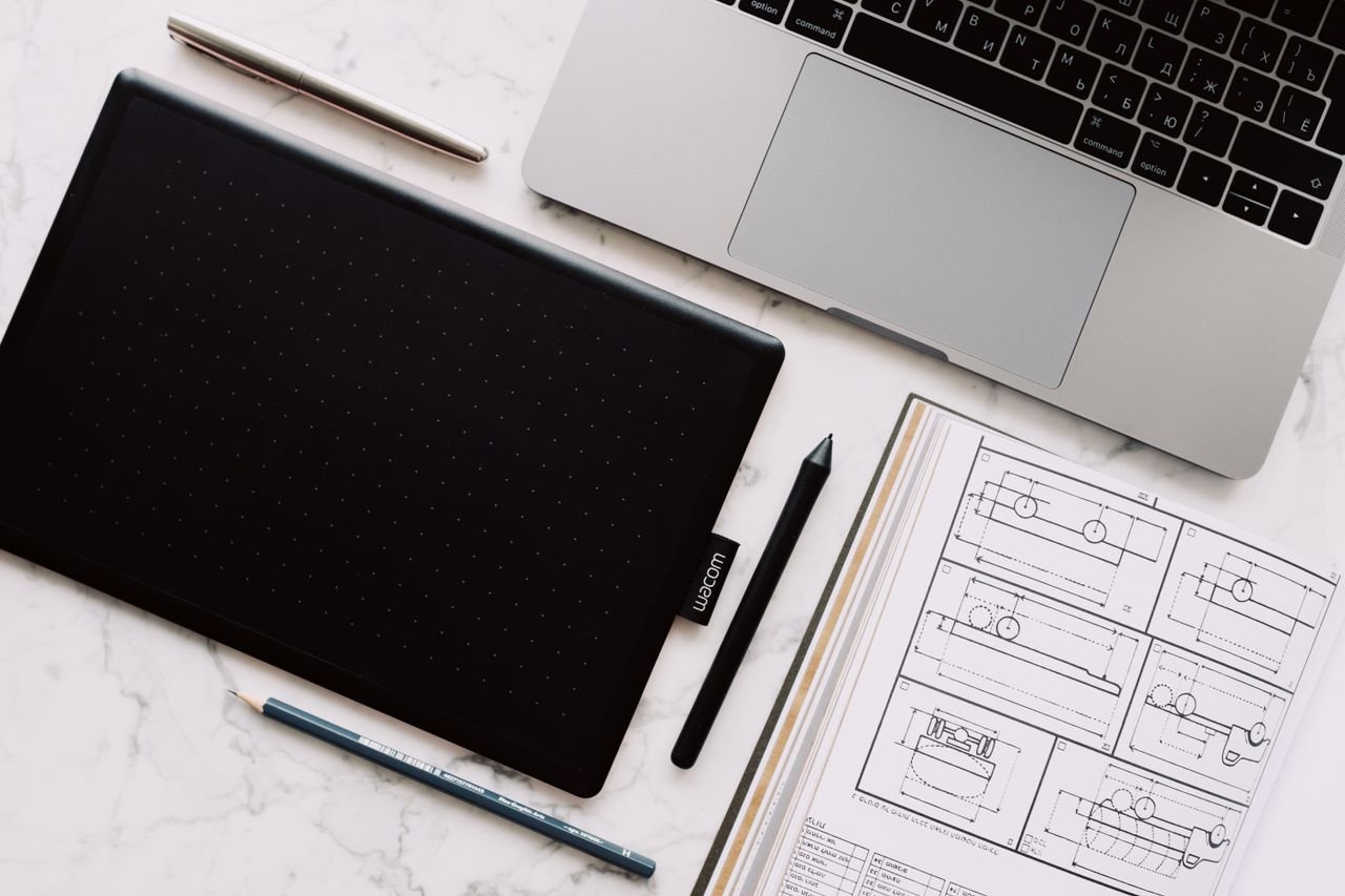 Top-down view of a desk setup including a laptop, drawing tablet, and design sketches.
