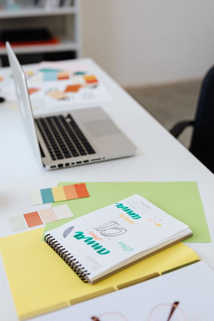Desk setup featuring laptop, notebooks, and colorful paper swatches for design inspiration.